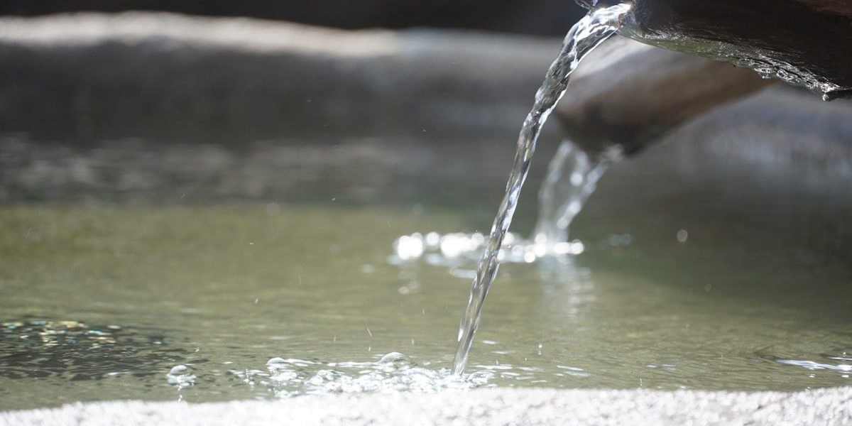 Clear water flows from a wooden spout into a pool
